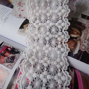 May include: White cotton lace trim with a scalloped edge and a delicate floral pattern. The lace is approximately 1 inch wide.