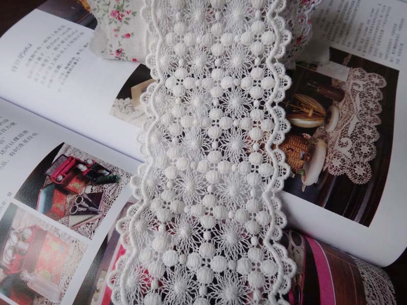 May include: White cotton lace trim with a scalloped edge and a delicate floral pattern. The lace is approximately 1 inch wide.