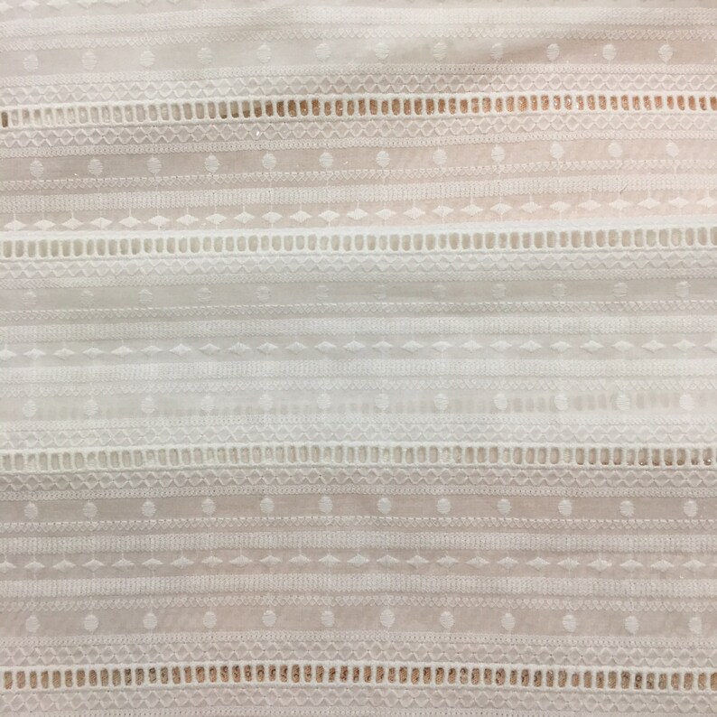 May include: White cotton fabric with a delicate embroidered pattern. The pattern features a repeating design of small circles, diamonds, and lines.