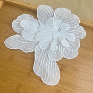 Può includere: Applique di fiore in tessuto bianco a strati con un design delicato e intricato. Questo abbellimento floreale è perfetto per aggiungere un tocco di eleganza a vestiti, accessori o progetti di arredamento per la casa.