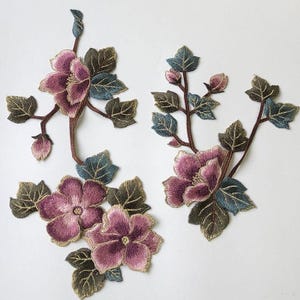 May include: Embroidered floral appliques featuring detailed purple and pink flowers with green and blue leaves. The appliques are attached to brown stems, creating a realistic and decorative design. Ideal for fabric embellishment.