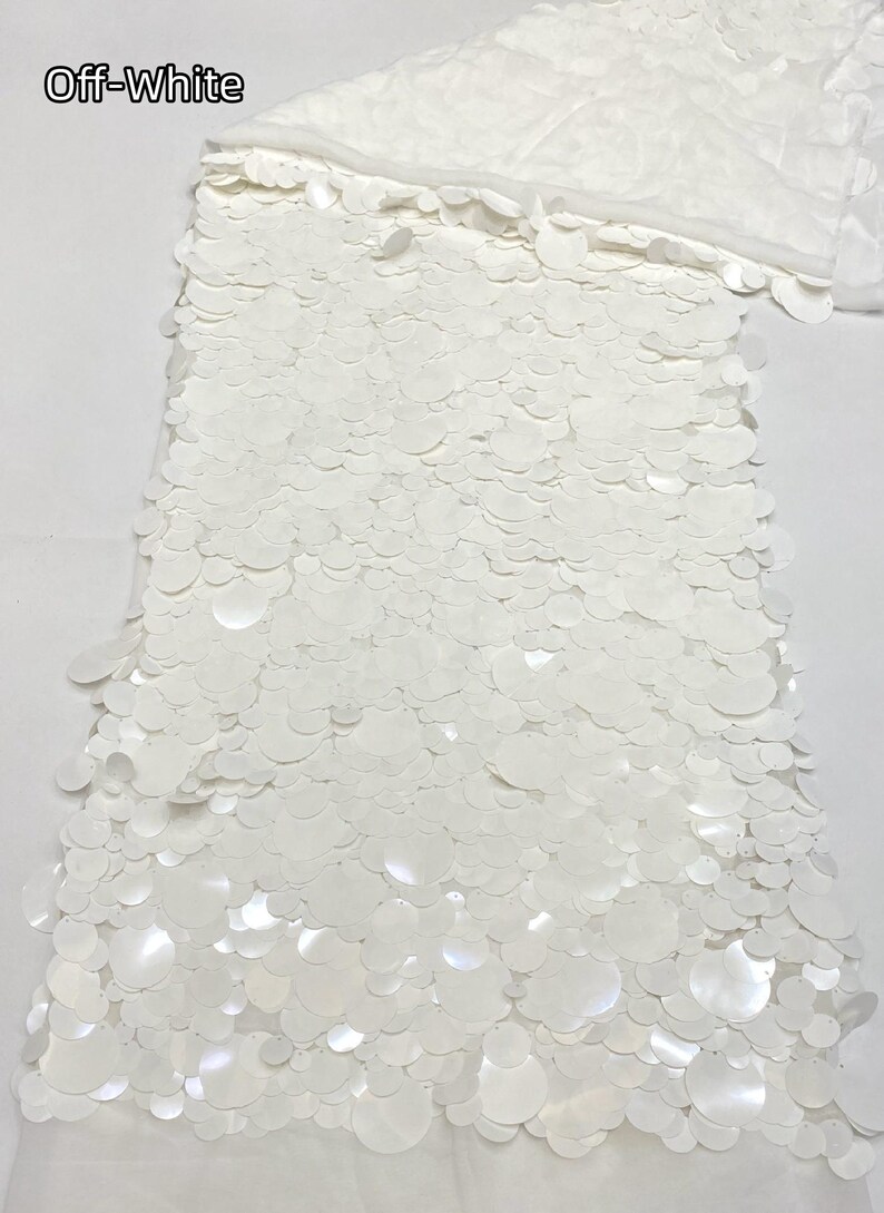 Puede incluir: Tela color blanco roto con una capa densa de lentejuelas circulares superpuestas de varios tama&ntilde;os. Las lentejuelas est&aacute;n fijadas sobre una base transparente, creando una superficie texturizada y reflectante de color uniforme.