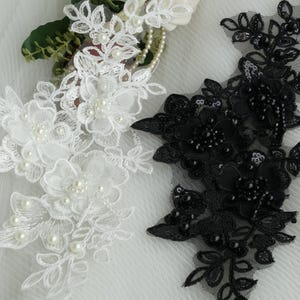 May include: Close-up of white and black floral lace appliques. The white applique features embroidered flowers and faux pearls. The black applique has sequins and beads. Both are on a sheer mesh backing, ideal for embellishing garments or crafts.