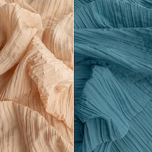 May include: A split image featuring two fabric samples. One side shows a soft, textured fabric in a light peach colour, while the other presents a similar fabric in a muted teal colour. The fabrics are draped, revealing their pleated texture.