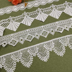 May include: Four distinct strips of white lace trim featuring varied patterns. The top strip has a scalloped edge, the second features fan-like shapes, the third displays diamond motifs with central stars, and the bottom has a floral scalloped border.