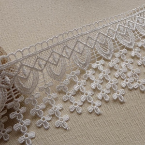 May include: White lace trim with a scalloped edge and a fringe of small flowers. The lace is delicate and intricate, with a floral pattern.