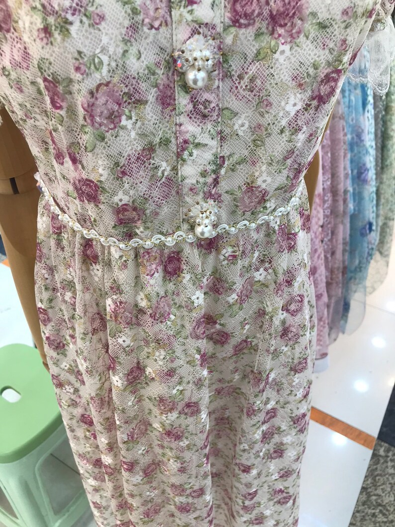 May include: A white lace dress with a floral print and a pearl and rhinestone embellishment at the waist.