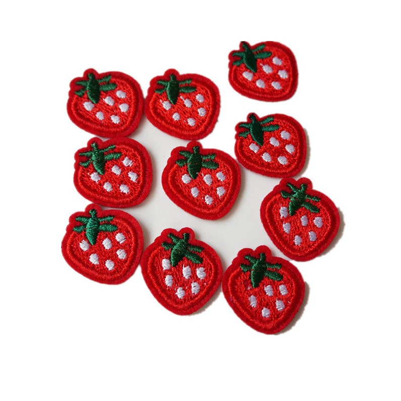 May include: A collection of ten embroidered strawberry patches. Each patch features a red strawberry with white seed details and a green stem. The patches are arranged on a white background, showcasing their vibrant colors and intricate stitching.