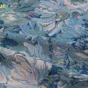 May include: A blue fabric featuring a woven floral pattern with shades of light blue, dark blue, and hints of muted green and cream. The textile displays a dense, textured weave with visible folds and the text A: blue in the upper left corner.