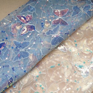 May include: Two pieces of sheer fabric with butterfly designs and iridescent sequins. The fabric on top is light blue and the fabric on the bottom is white.