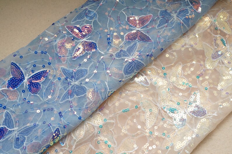 May include: Two pieces of sheer fabric with butterfly designs and iridescent sequins. The fabric on top is light blue and the fabric on the bottom is white.