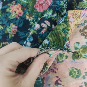 Puede incluir: Una tela tejida con un denso patr&oacute;n floral de flores rosas, verdes y azules sobre un fondo negro en un lado, mientras que el reverso muestra un dise&ntilde;o floral m&aacute;s claro en tonos melocot&oacute;n y verde con una costura visible.