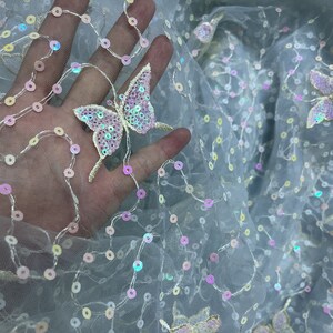 May include: Pale blue tulle fabric with iridescent sequins and embroidered butterflies. The butterflies are made of sequins and have a pink and purple colour scheme.
