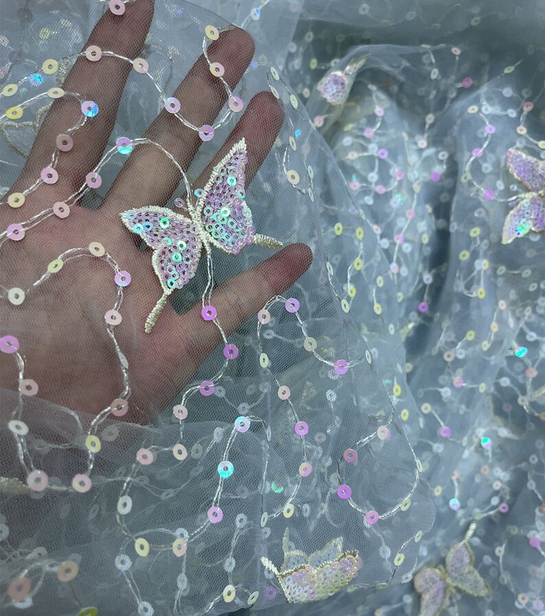 May include: Pale blue tulle fabric with iridescent sequins and embroidered butterflies. The butterflies are made of sequins and have a pink and purple colour scheme.