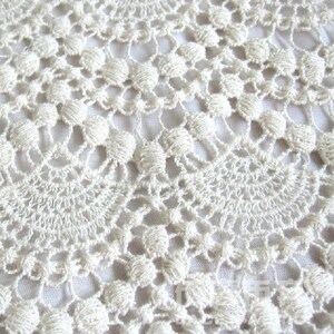 May include: Close-up of a white crocheted lace fabric with a delicate pattern.