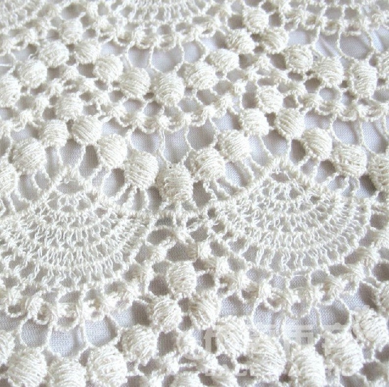 May include: Close-up of a white crocheted lace fabric with a delicate pattern.