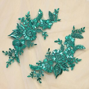 May include: Two emerald green floral lace appliques featuring intricate embroidery and shimmering sequins. Each piece displays a detailed botanical design with leaves and blossoms, crafted on a sheer mesh backing for garment embellishment.
