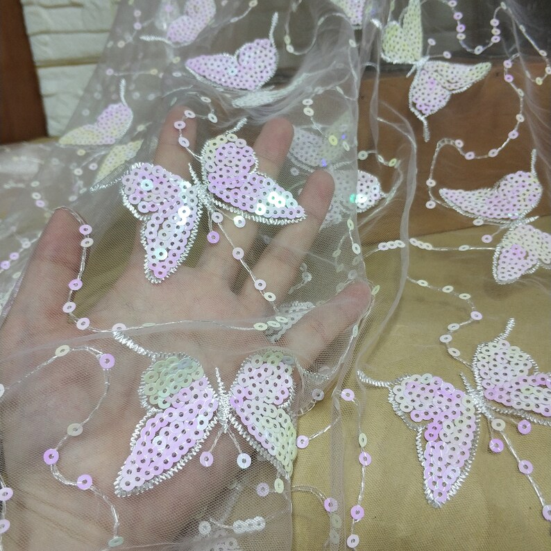 May include: White sheer fabric with iridescent pink and white butterfly sequins. The fabric is delicate and has a soft, flowing texture.