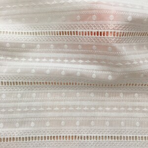 May include: White cotton fabric with a delicate embroidered pattern of circles, diamonds, and lines. The fabric has a slightly textured surface.