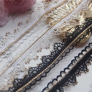 Puede incluir: Cuatro diferentes galones de encaje con abalorios dorados. Dos galones son blancos y dos galones son negros.