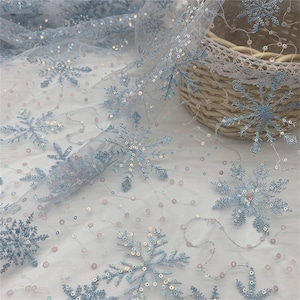 May include: White tulle fabric with blue snowflake embroidery and iridescent sequins. The fabric is sheer and delicate, perfect for crafting or decorating.