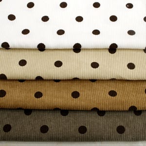 May include: Four stacked layers of corduroy fabric, each featuring a repeating dark brown polka dot pattern. The fabric colors range from white to beige, light brown, and dark gray, all displaying a distinct vertical ribbed texture.