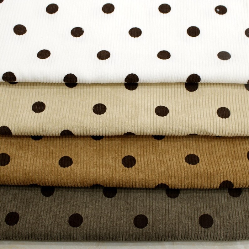 May include: Four stacked layers of corduroy fabric, each featuring a repeating dark brown polka dot pattern. The fabric colors range from white to beige, light brown, and dark gray, all displaying a distinct vertical ribbed texture.