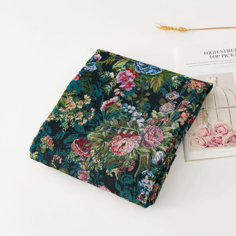 Puede incluir: Una pieza de tela oscura doblada que presenta un denso patr&oacute;n floral tejido en tonos rosa, rojo, azul y verde. El textil muestra un complejo dise&ntilde;o bot&aacute;nico con diversas formas de flores y follaje, sobre un fondo de color negro intenso.
