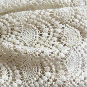 May include: Close-up of a white crocheted fabric with a delicate pattern of circles and loops.