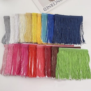 Pode incluir: Uma coleção de acabamentos de franjas coloridas em várias tonalidades, incluindo cinza, branco, amarelo, azul, rosa, vermelho, marrom e verde. A franja é feita de um material fino em forma de fio e é disposta em fileiras ordenadas. A imagem é bem iluminada.