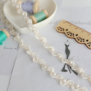 May include: White beaded trim with a delicate, scalloped design. The trim features small, round pearls and a subtle shimmer.
