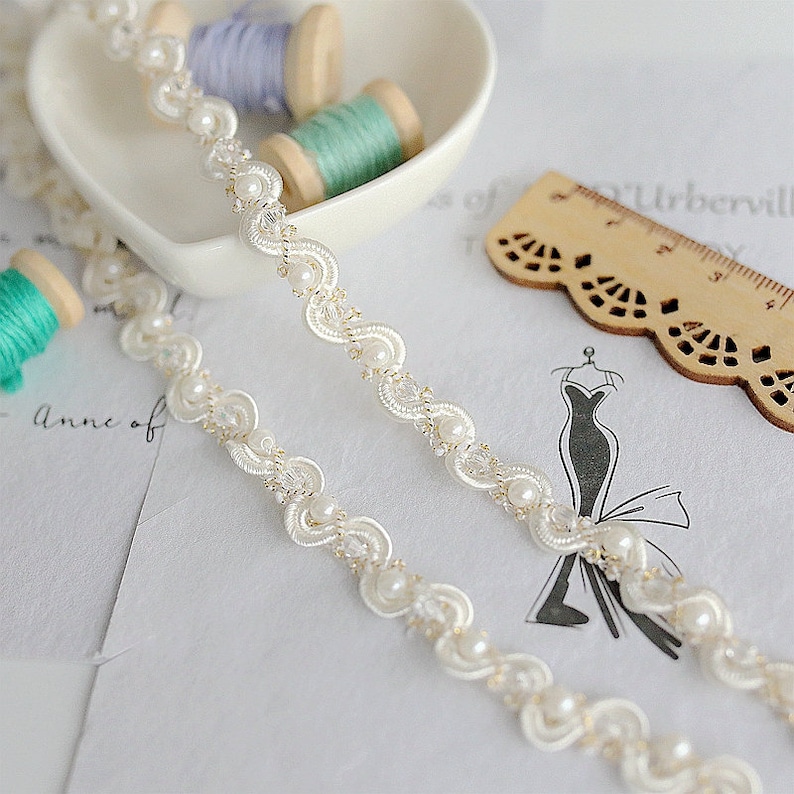 May include: White beaded trim with a delicate, scalloped design. The trim features small, round pearls and a subtle shimmer.