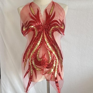 以下が含まれることがあります： 装飾的なデザインの、透け感のある薄いピンク色の衣服。赤と金のスパンコールの装飾が、対称的で流れるようなパターンで施されています。マネキンに着せられており、その形とディテールが示されています。