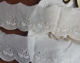 May include: White cotton lace trim with a scalloped edge and embroidered floral designs. The lace is shown on a white surface.
