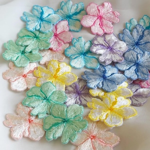 Op de afbeelding: Een verzameling geborduurde bloem applicaties in diverse pastelkleuren, waaronder roze, blauw, geel en groen. Elke bloem heeft gedetailleerde steken en een delicate uitstraling, perfect voor knutselen of het verfraaien van stoffen.