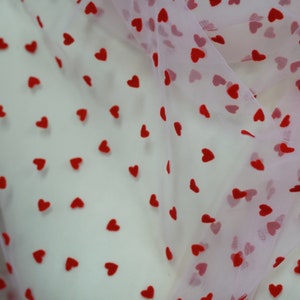 May include: Pink tulle fabric with red heart-shaped patterns. The fabric is sheer and delicate, with a soft, romantic feel.