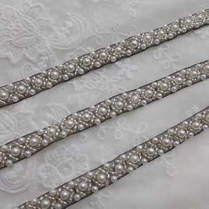 May include: Three rows of black ribbon trim with white pearl beads sewn in a geometric pattern.