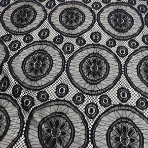 Peut inclure: Un tissu en dentelle noire pr&eacute;sentant un motif r&eacute;p&eacute;titif de grands cercles avec des centres floraux complexes. Le design comprend de plus petits accents circulaires intercal&eacute;s entre les grands cercles, reli&eacute;s par une fine maille ajour&eacute;e.