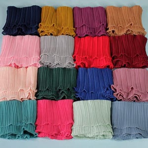 May include: A collection of pleated fabric pieces in various colors, including navy, yellow, pink, gray, red, and teal. Each piece has a ruffled edge, creating a layered effect. The fabric appears to be lightweight and suitable for clothing or craft projects.