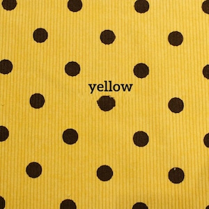 May include: A bright yellow corduroy fabric featuring a repeating pattern of dark brown polka dots. The word yellow is printed in black lowercase letters in the center of the fabric, positioned directly over one of the dark brown polka dots.