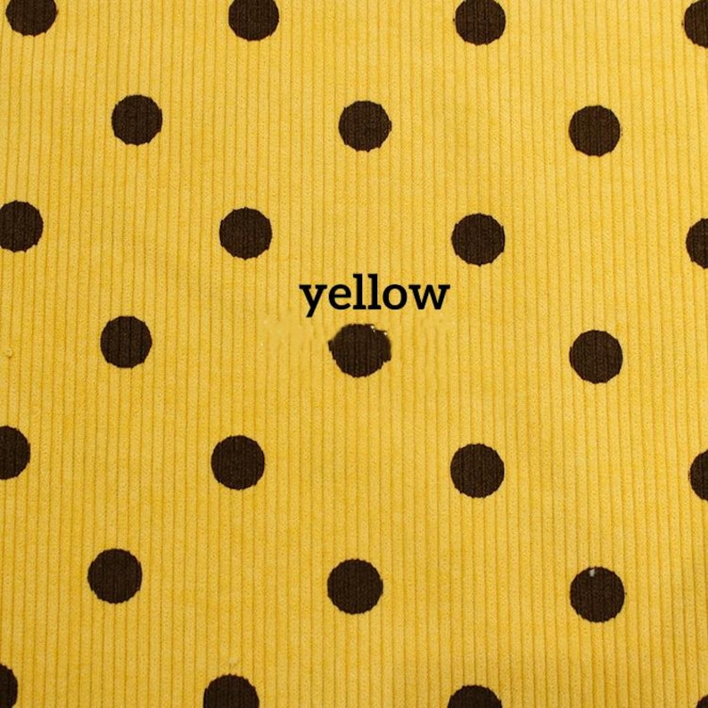 May include: A bright yellow corduroy fabric featuring a repeating pattern of dark brown polka dots. The word yellow is printed in black lowercase letters in the center of the fabric, positioned directly over one of the dark brown polka dots.