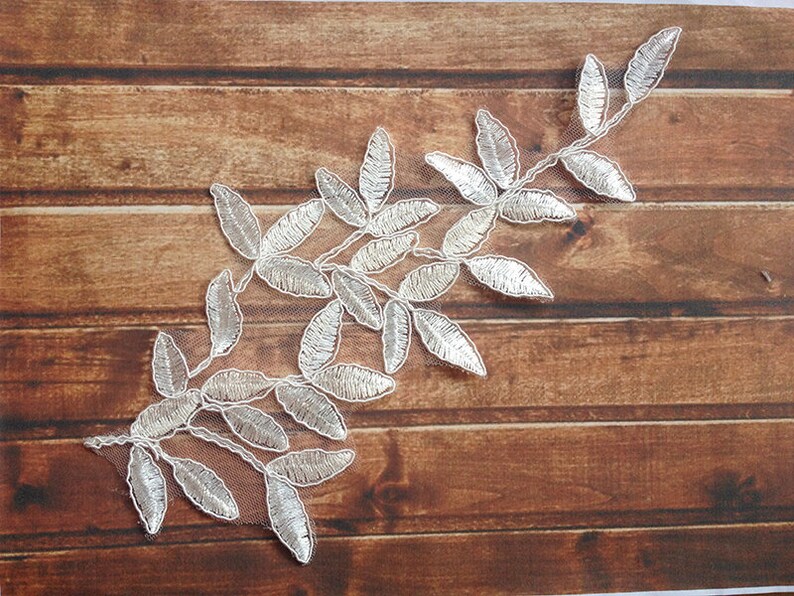 May include: A silver leaf lace applique with a delicate floral design. The lace is on a white mesh background and is perfect for adding a touch of elegance to any project.