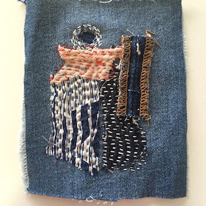 Könnte beinhalten: Ein kleines Stück Jeansstoff mit verschiedenen Stoffresten, die darauf genäht sind. Die Stoffreste sind in Blautönen, Weiß und Rot gehalten und haben verschiedene Muster, darunter Streifen, Punkte und geometrische Muster.