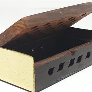 May include: A small, open wooden box with a hinged lid. The box is dark brown with gold-colored accents on the front and a black interior. The lid has decorative cutouts and is slightly ajar.