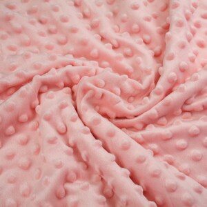 May include: Close-up of a soft, pink fabric with a textured, dotted pattern. The fabric is wrinkled and folded, showing the texture of the material.
