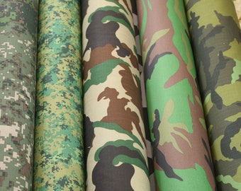 Könnte beinhalten: Eine Sammlung gerollter Tarnstoffe in verschiedenen Mustern. Die Muster umfassen digitale und traditionelle Walddesigns in Grün-, Braun- und Beigetönen. Der Stoff scheint dicht gewebt zu sein.