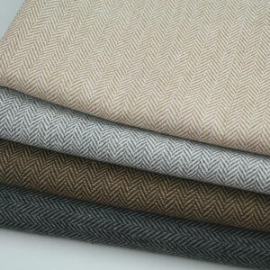 Könnte beinhalten: Nahaufnahme von vier gefalteten Stoffen in neutralen Farbtönen. Die Stoffe sind beige, grau, braun und dunkelgrau, jeweils mit einem Fischgrätmuster. Die Texturen wirken weich und eignen sich für Kleidung oder Heimdekoration.