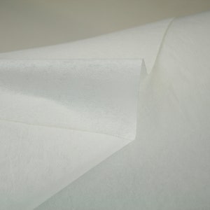 May include: White fabric with a smooth, slightly textured surface. The fabric is folded in half, creating a sharp crease.