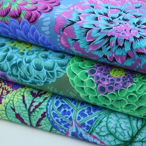 Op de afbeelding: Close-up van gevouwen stof met grote, gestileerde bloempatronen. De ontwerpen tonen levendige kleuren, waaronder tinten blauw, blauwgroen, paars en groen. De stof lijkt gelaagd te zijn en onthult de ingewikkelde details van de bloemenprints.