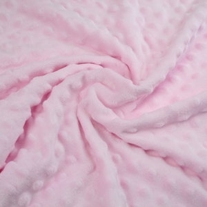 May include: A soft, pink fabric with a textured, dotted pattern. The fabric is folded and draped, showing its texture and colour.